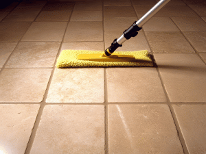 A tile floor is being mopped with a flat mop. The tile is light brown with grey grout, appearing clean.