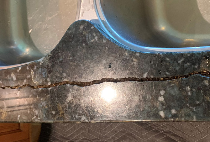 This granite countertop is cracked. The crack runs along the front edge of the kitchen sink.