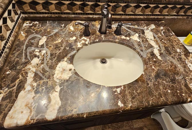 A marble vanity has been chemically damaged by improper cleaners.